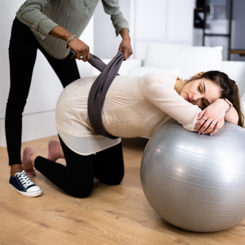A doula helps a pregnant person near an exercise ball