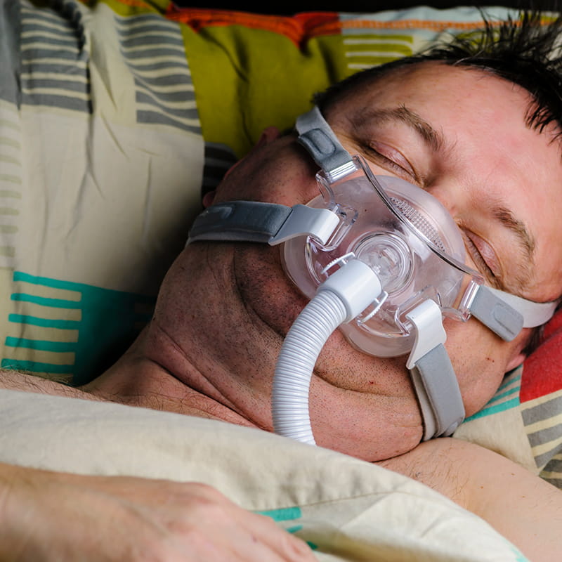 Middle aged overweight man wears a CPAP to help him sleep due to sleep apnea