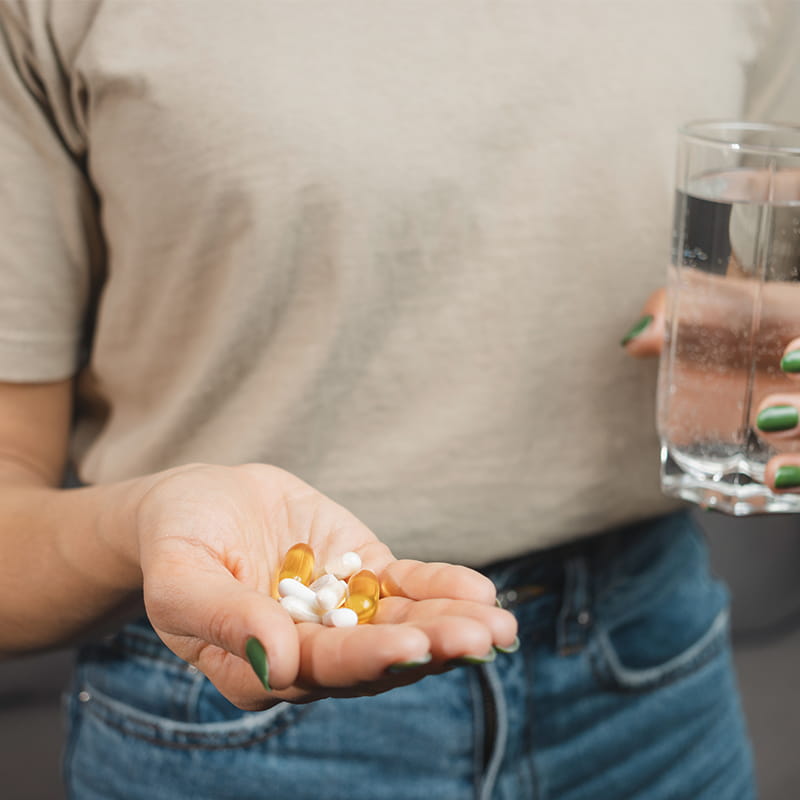 Young woman holds various medical pills and capsules in a hand and glass of water, close-up view