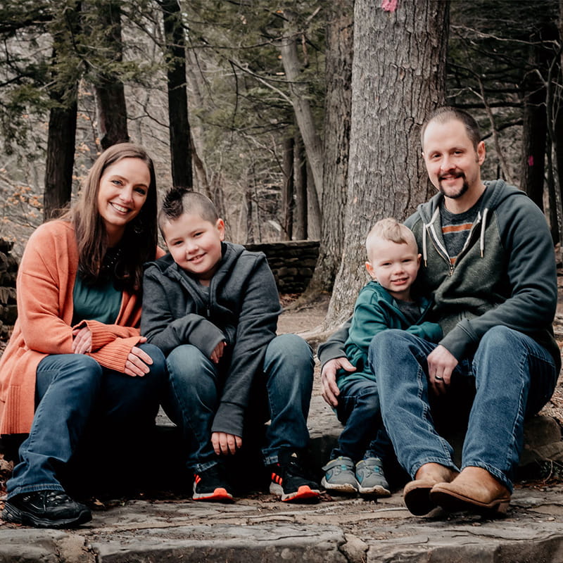 Mom and dad and two young boys in the woods smiling